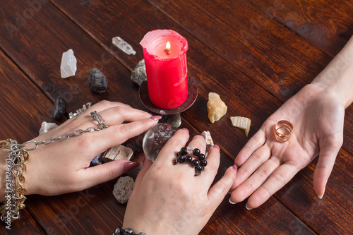 A Gypsy woman performs a love spell. A clairvoyant palmist reads by hand with a candle. A fortune teller predicts the fate of love with wedding rings, a magic ball, lighted candles and magic stones. photo