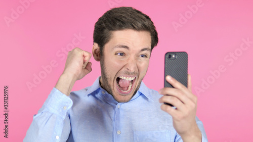 Young Man Celebrating Success while Using Smartphone on Pink Background