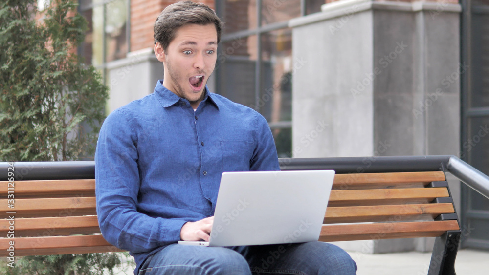 Sitting Outdoor Young Man in Shock Working on Laptop Sitting Outdoor Young Man in Shock Working on Laptop