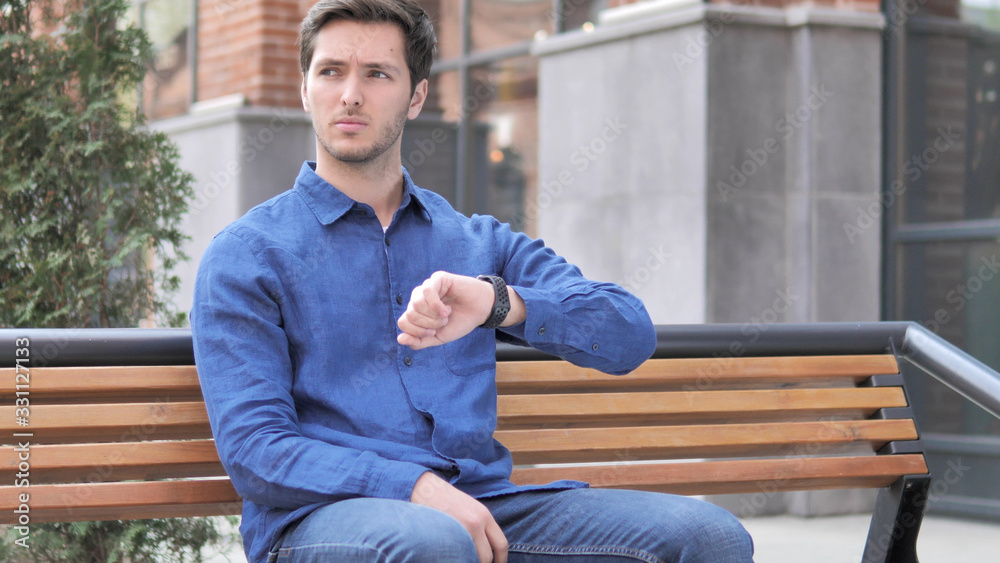 Waiting Young Man Watching Time on Watch, Sitting on Bench Waiting Young Man Watching Time on Watch, Sitting on Bench