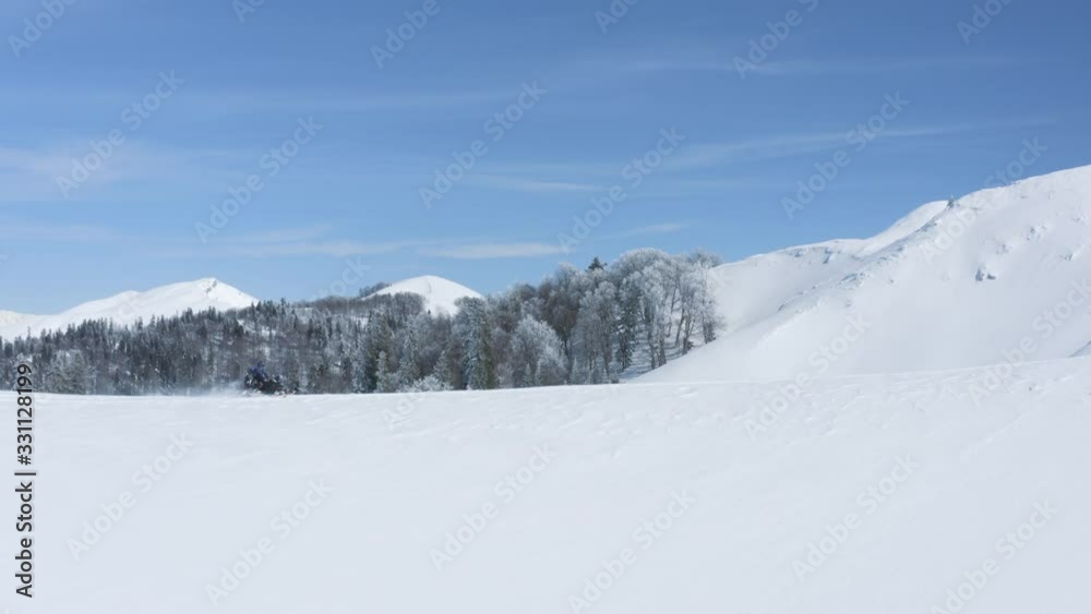 People riding on snowmobile on snowy highlands with snow fir forest at sunny winter day. Snowboarders driving on snowmobile on winter mountain resort. People riding on snowmobile on snowy highlands with snow fir forest at sunny winter day. Snowboarders driving on snowmobile on winter mountain resort.