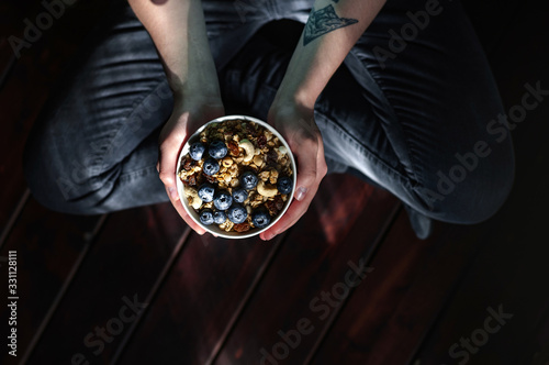 Hands holding cup with granola and berries.