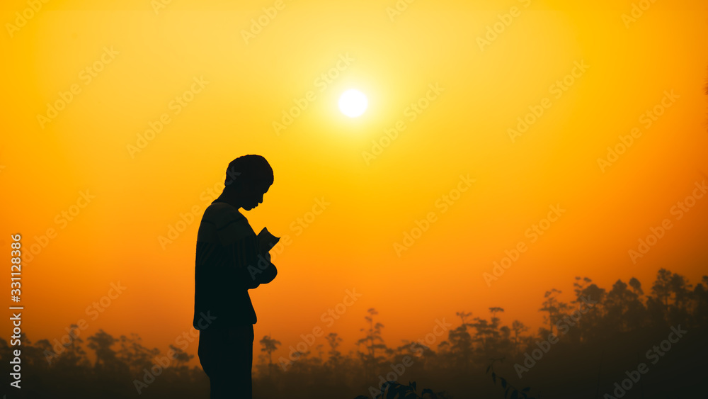 Human standing and hugging Bible with light sunset background, christian silhouette concept.