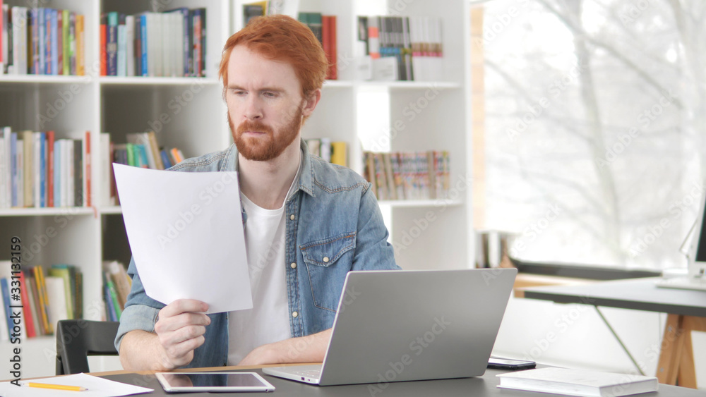 Young Casual Redhead Man Reading Contract at Work Young Casual Redhead Man Reading Contract at Work