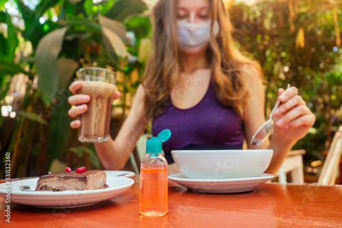 woman useing antibacterial gel on hands before start to eating her healthy food in tropical asian cafe . smoothie bowl , raw cake and coffee on table with sanitizer on bottle © yurakrasil