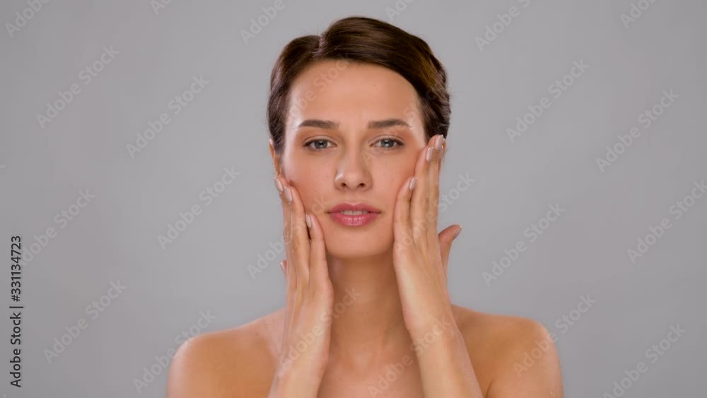 beauty, bodycare and people concept - beautiful young woman touching her face over grey background beauty, bodycare and people concept - beautiful young woman touching her face over grey background