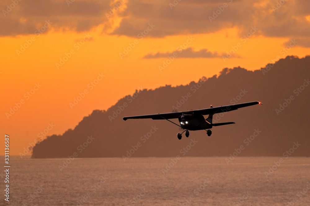 Aircraft on the orange sky with dark clouds. Airplane in the wil nature. Forest hill near the ocean water. Air travelling in Costa Rica. Evening sunset in sea coast of Corcovado NP, Costa Rica.