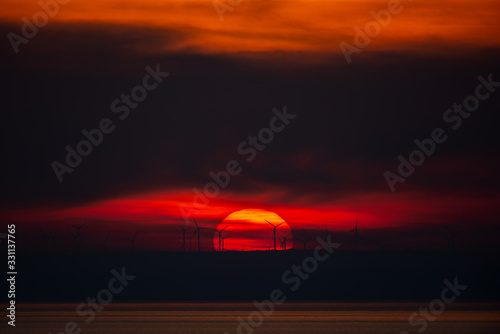 Sun setting behind wind turbines with clouds around © Adi