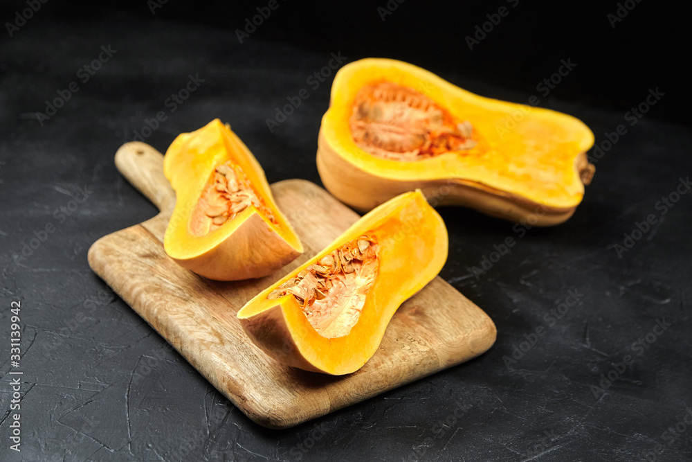 Butternut squash pieces with seeds on wooden cutting board on black background, closeup. Pumpkin seeds. Cooking winter squash