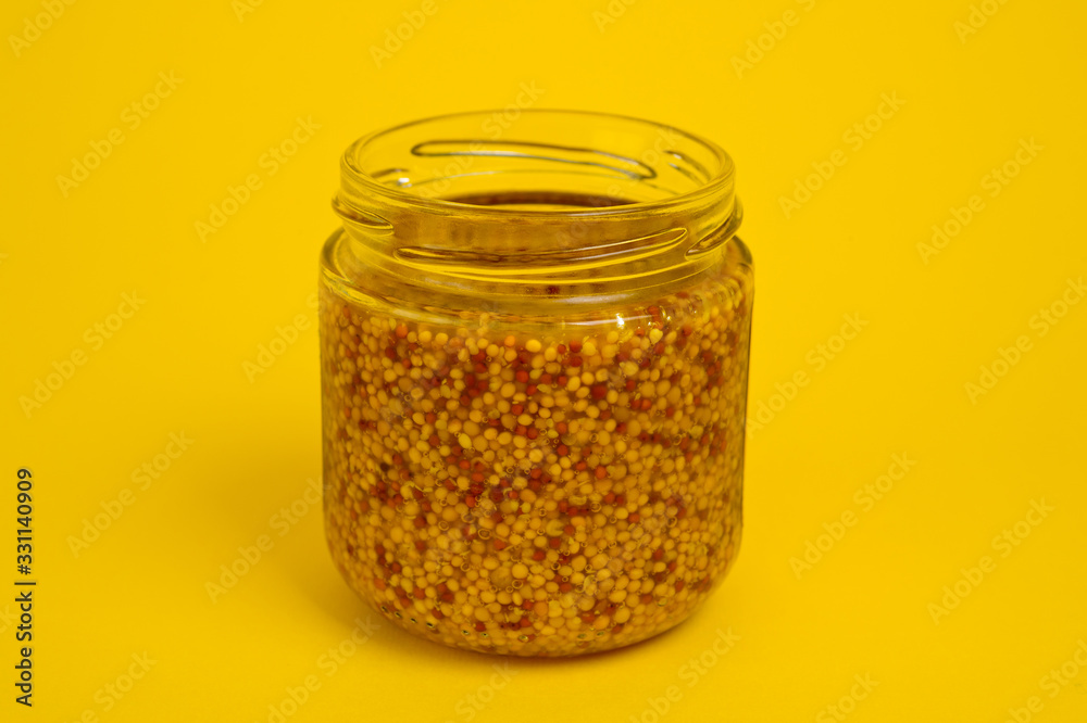 French mustard in a glass jar, shot on a yellow background. Background for seasoning and nutrition. French mustard in a glass jar, shot on a yellow background. Background for seasoning and nutrition.
