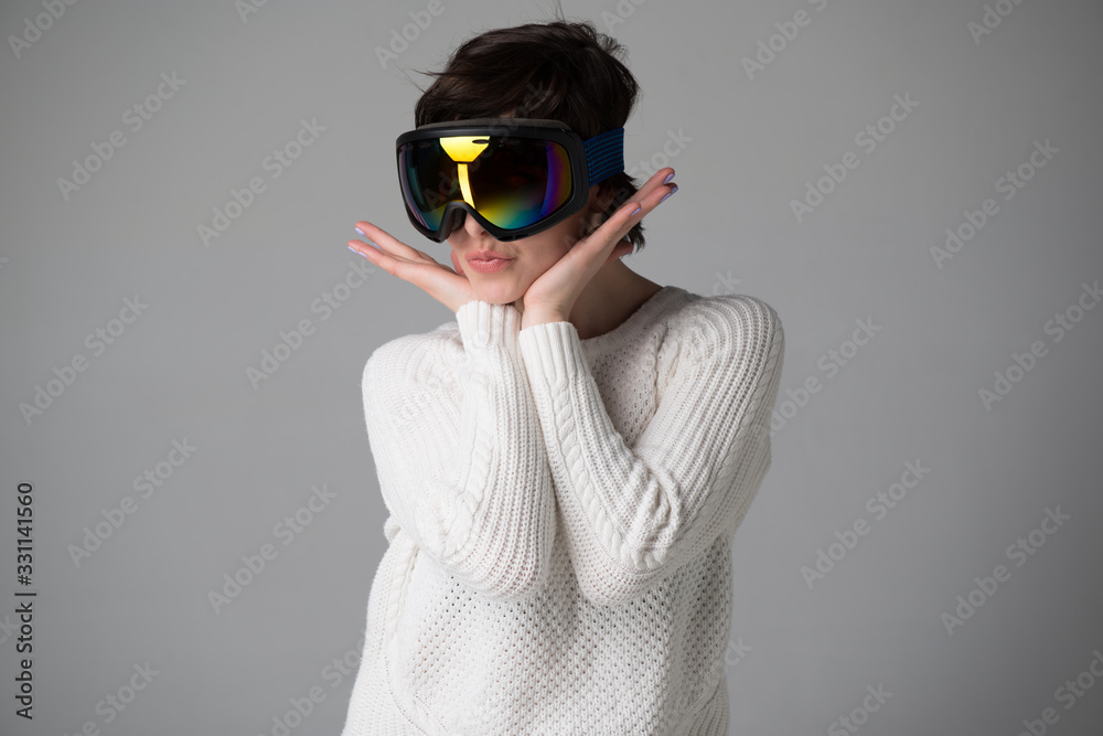 Female portrait in ski goggles with positive expressions. Beautiful young woman happy and excited expressing winning gesture over gray background. Girl and  snow winte sport equipment theme