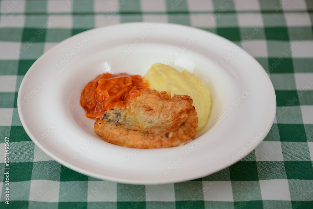 Fried fish filet with mashed potatoes and tomato sauce served on white plate on wooden table. Fried fish filet with mashed potatoes and tomato sauce served on white plate on wooden table.