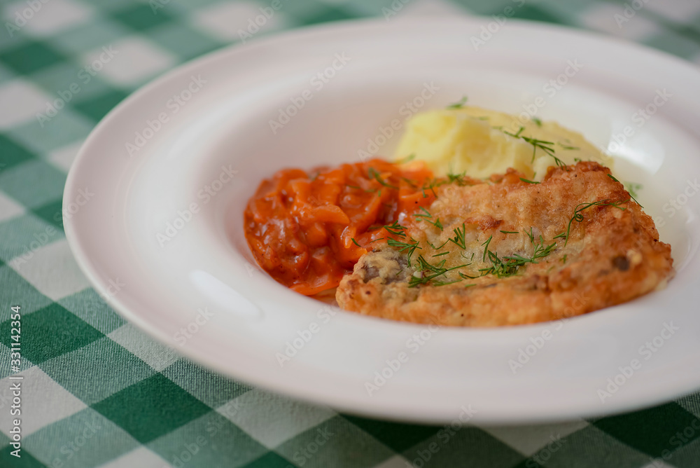 Fried fish filet with mashed potatoes and tomato sauce served on white plate on wooden table.