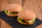 Two hamburgers on the rustic wooden table on black board. Fast food, junk food concept. Food photography concept.