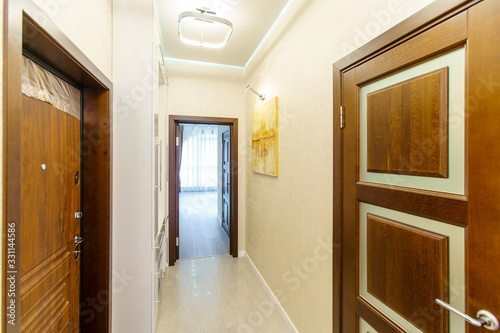 a long corridor in the apartment with beige Wallpaper  numerous doors and light yellow abstract paintings on the walls