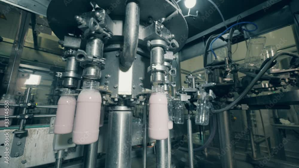 Revolving conveyor is pouring milk substance into bottles Revolving conveyor is pouring milk substance into bottles
