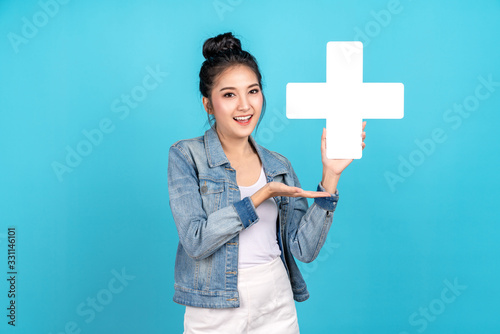 Happiness asian woman smiling, showing plus or add sign and other hand open on blue background. Cute asia girl wearing casual jeans shirt and showing join sign for increse and more benefit concept