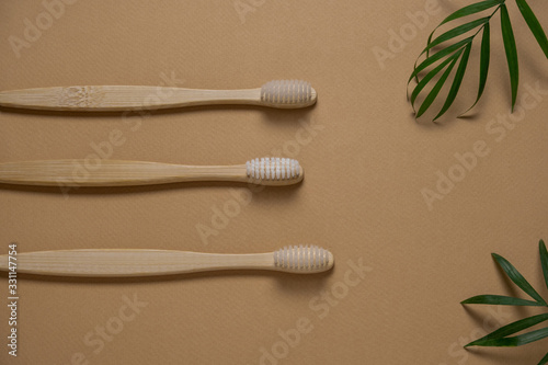 top view three  eco friendly wooden tooth brushes and green tropical leaves layout on a light brown background © dvulikaia