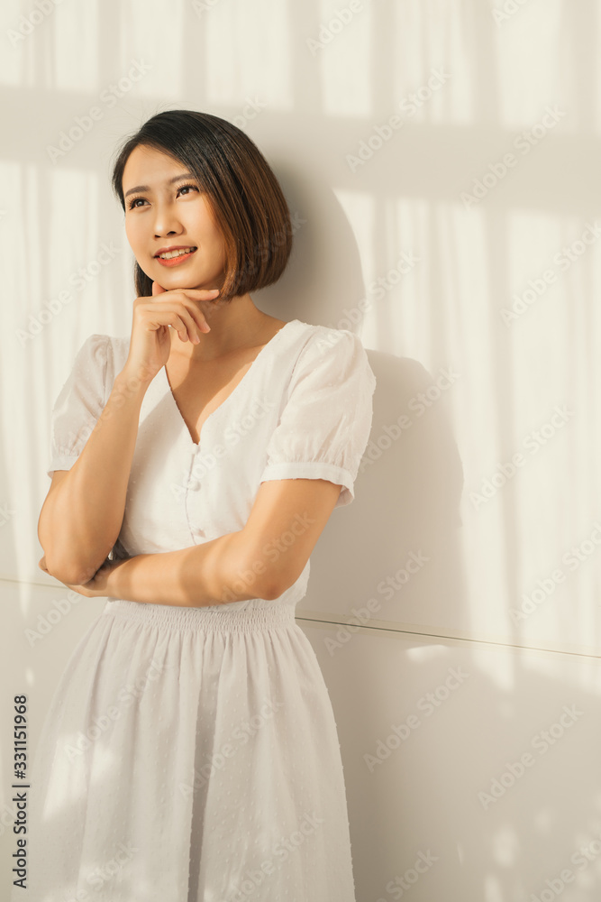A young beautiful is standing against the wall, the sunlight is beautifully falling. Shade from the blinds. A young beautiful is standing against the wall, the sunlight is beautifully falling. Shade from the blinds.