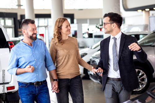 Fototapeta Naklejka Na Ścianę i Meble -  Young sales agent helping adult couple to choose a new car in modern car showroom.