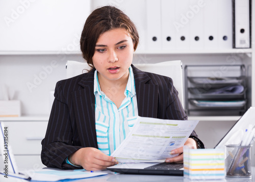 Female office worker is reading documents about the transaction © JackF