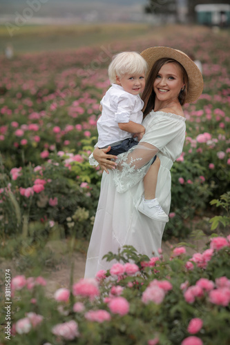 A woman with a child in her arms stands in a field with blossoming roses.