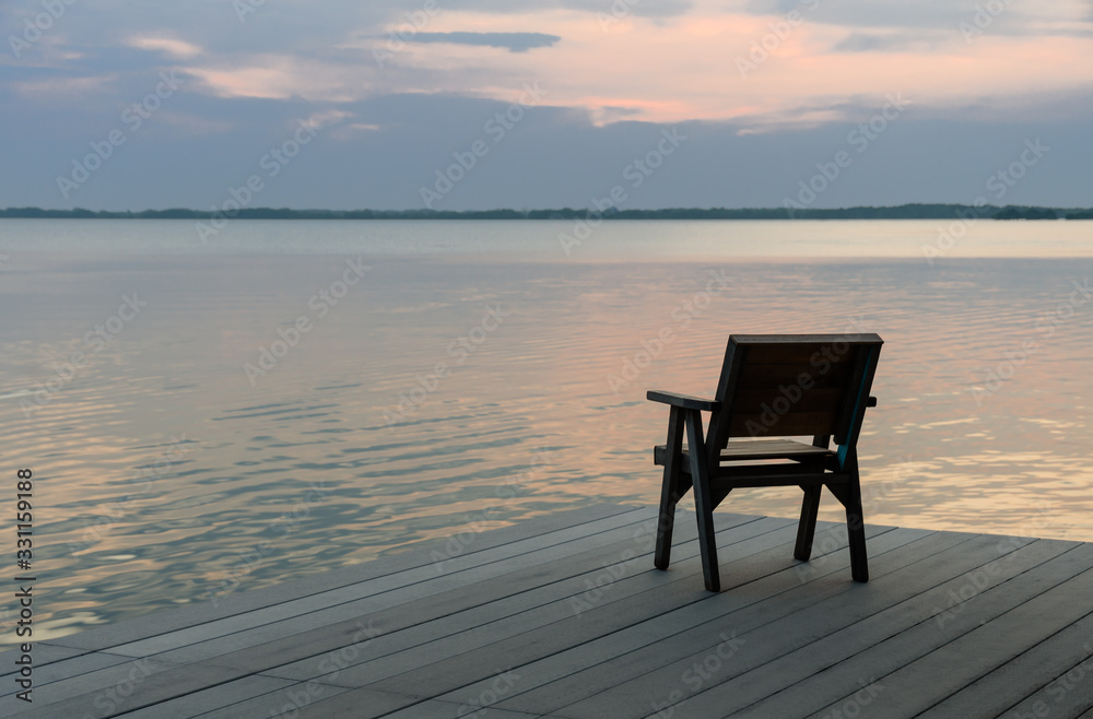 Wooden chair on a wood pier overlooking calm lake at sunset skyline. Wooden chair on a wood pier overlooking calm lake at sunset skyline.