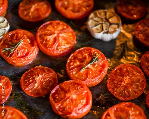 Baked halves of tomatoes with garlic and rosemary on baking paper in the oven. Dish. Cook at home. Close-up. View from above. Slices of tomato.