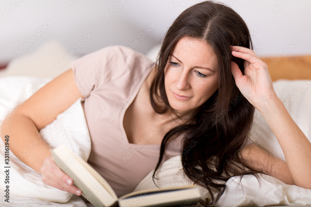 dunkelhaarige frau liest im schlafzimmer ein buch