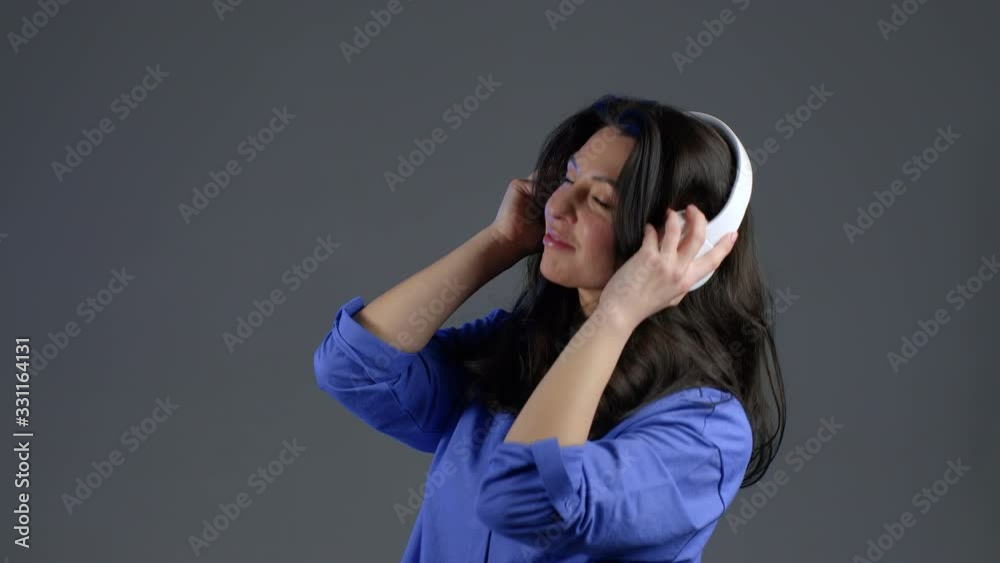 Attractive european adult woman with long hair dancing with headphones on grey studio background. Cute ladys portrait. Music, radio, happiness, freedom, youth concept. Attractive european adult woman with long hair dancing with headphones on grey studio background. Cute ladys portrait. Music, radio, happiness, freedom, youth concept.