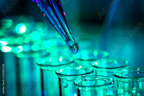 Pipette adding fluid to one of several test tubes, medical abstract background.