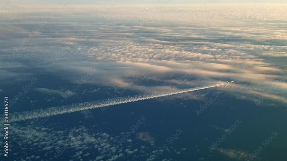 Unusual aerial view of airplane flying high above clouds leaving air trail Unusual aerial view of airplane flying high above clouds leaving air trail