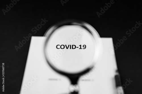 Pandemia COVID-19, napis powiększony przez lupe, strzykawka, stetoskop na ciemnym tle