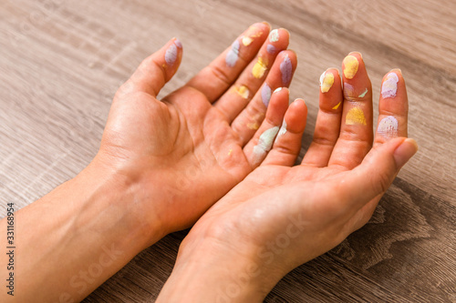 easter and feminity concept. closeup woman hands dirty by goache paint with multicolor spots over a wooden table