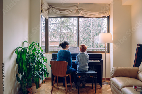 Mom teaching her son at home piano lessons. Family lifestyle spending time together indoors. Children with musical virtue and artistic curiosity. Educational musical activities for little kid.