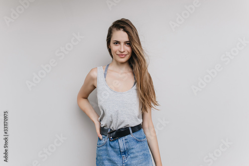 Enchanting long-haired girl posing with pleased face expression. Indoor portrait of confident brunette young lady in denim skirt.