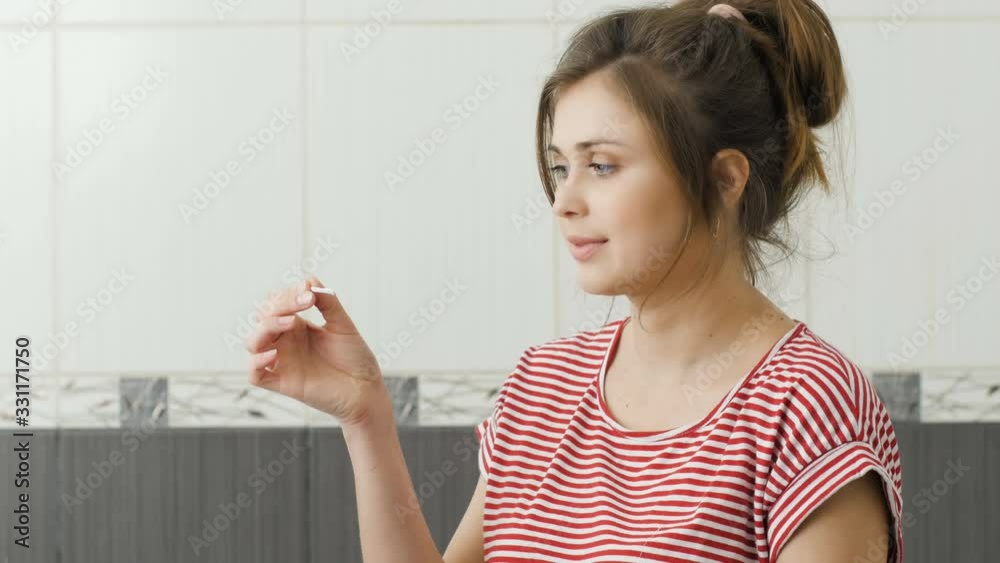 young smiling woman on pink studio background holds negative pregnancy test in her hand, girl is happy and showing thumb up, family planning concept