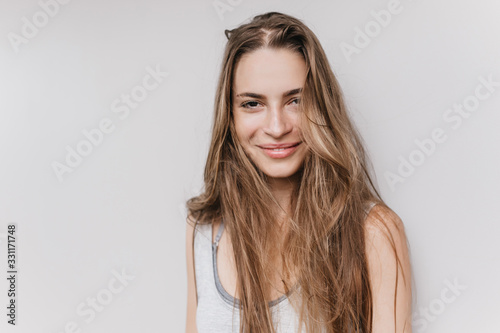 Fascinating young woman with cute smile posing in studio. Indoor photo of lovable female model with long shiny hair.