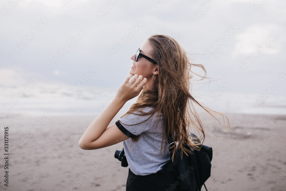 Gorgeous female photographer in gray t-shirt looking at cloudy sky. Outdoor portrait of romantic brunette girl with camera having fun at beach in cold day. Gorgeous female photographer in gray t-shirt looking at cloudy sky. Outdoor portrait of romantic brunette girl with camera having fun at beach in cold day.