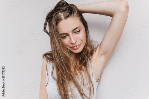 Slim wonderful lady playing with her long hair and looking away. Indoor photo of ecstatic caucasian girl isolated on light background with inspired face expression.