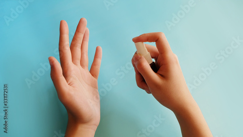 A hand holding a small spray bottle, spraying the content towards the other palm at some distance away.