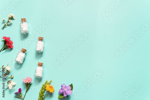 Homeopathic globules​ bottle with wildflowers​ on green backgound. Homeopathy alternative medicine concept. Flat​ layout. Copy space.