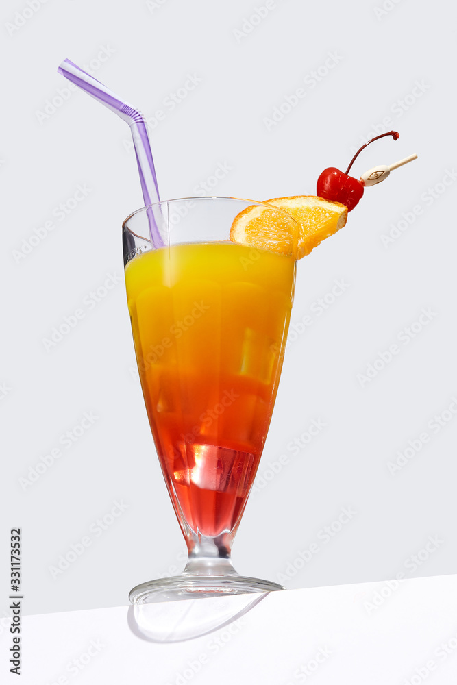 Sex on the Beach cocktail with ice cubes is contained in a milkshake glass with a straw, an orange slice and a cherry on the stick. The showy illustrative picture is made on the gray backdrop. Sex on the Beach cocktail with ice cubes is contained in a milkshake glass with a straw, an orange slice and a cherry on the stick. The showy illustrative picture is made on the gray backdrop.