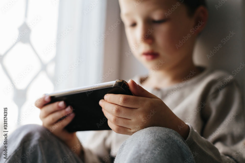 Toddler boy using tablet or smartphone. Cute five years old boy sitting at home using digital device. Toddler boy using tablet or smartphone. Cute five years old boy sitting at home using digital device.