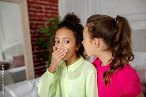 Dark-haired girl listening to her friend and looking shocked