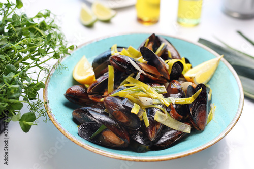 Mussels with leek and white wine. A tasty crustacean dish. A plate with an appetizing dish. Application suggestion. Culinary photography, food stylization.