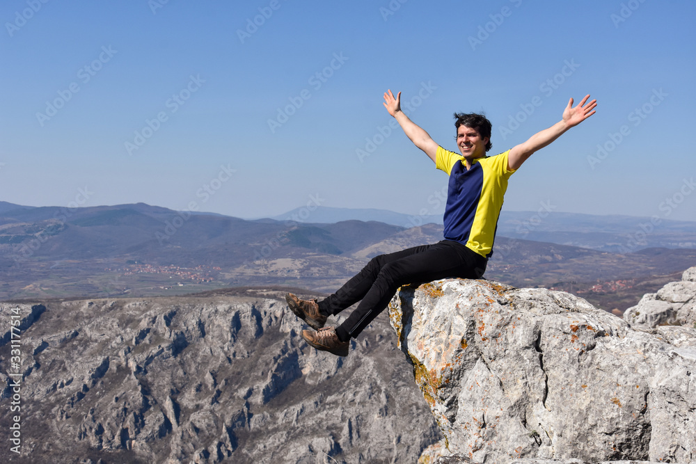 Man rise a hands on top of the mountain. Concept of freedom. Young man enjoy on a cliff edge Man rise a hands on top of the mountain. Concept of freedom. Young man enjoy on a cliff edge