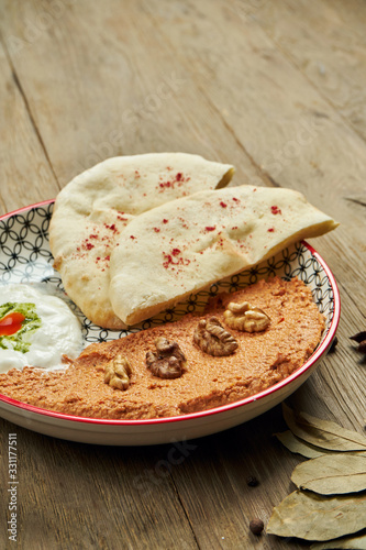 Muhammara is a classic eastren dish. baked pepper and walnut puree with Bazlama and yogurt in a ceramic plate on a wooden background. photo