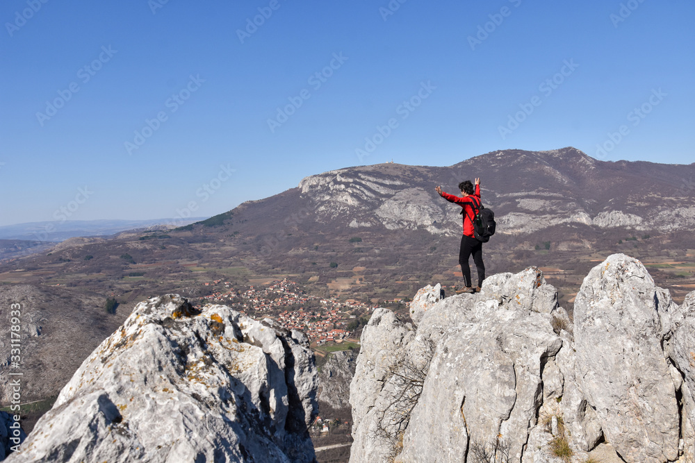 Man on a cliff with a gorgeous view on a village in mountain. Concept of freedom. Young man enjoy on a cliff edge