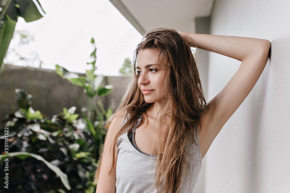 Brown-haired girl posing with dreamy face expression near white wall. Pensive caucasian lady touching her long hair and looking away. Brown-haired girl posing with dreamy face expression near white wall. Pensive caucasian lady touching her long hair and looking away.
